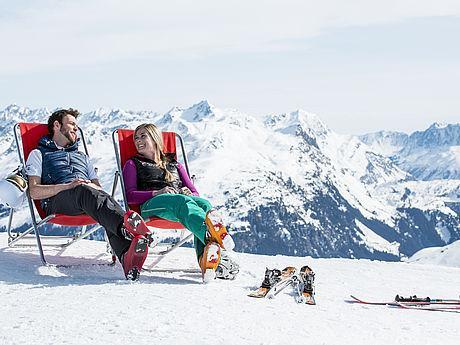 Skifahrer, sitzend in Liegestühlen vor dem Bergpanorama